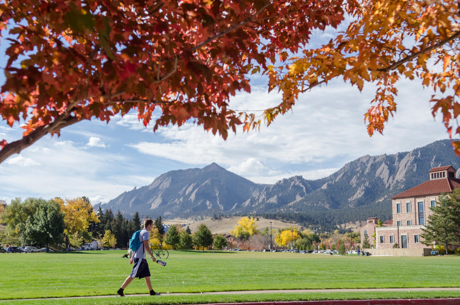 A student walks on a sidewalk in front of the Leeds Business School at the University of Colorado Boulder on a fall day